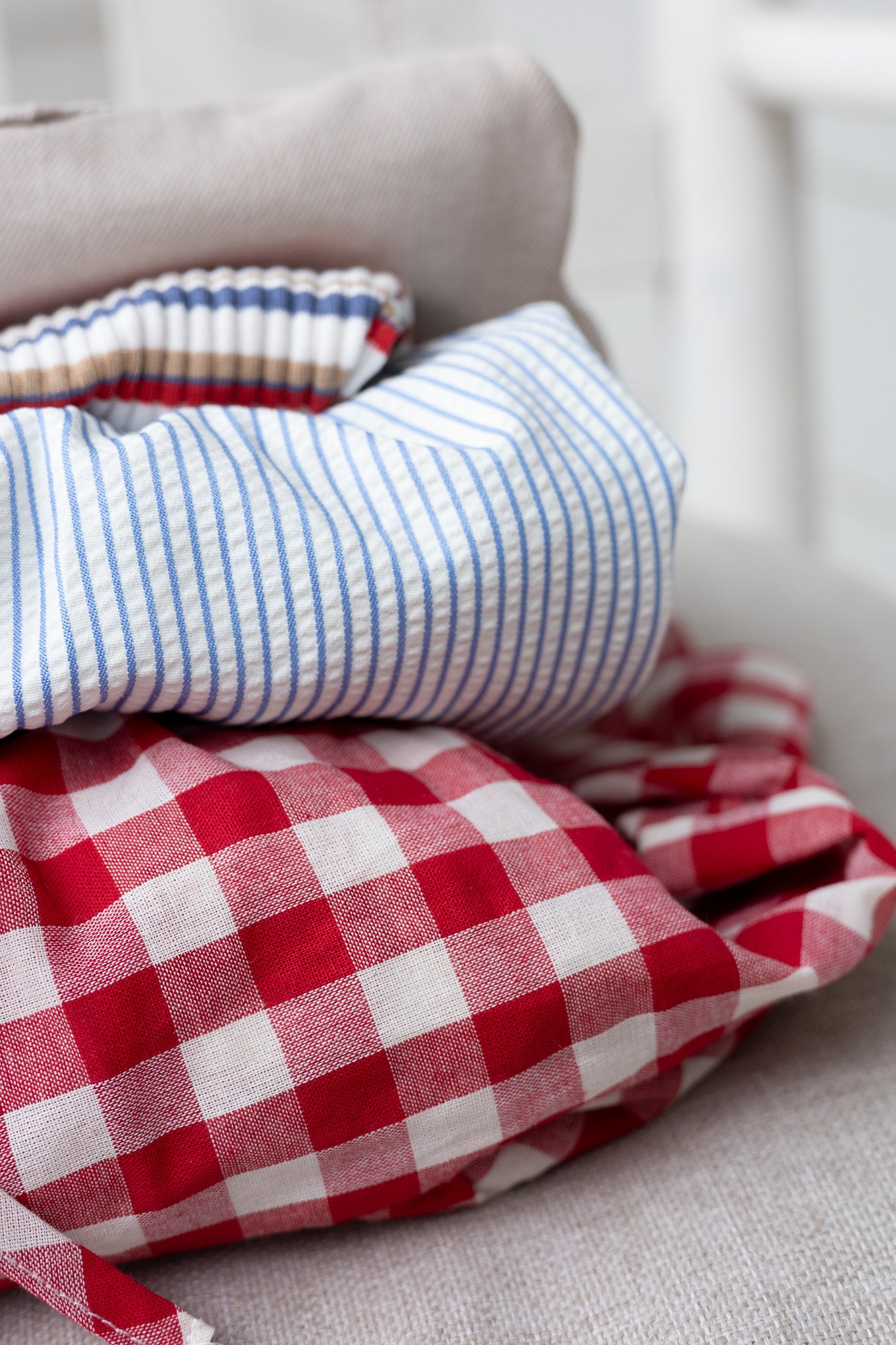 folded view Rowan Seersucker Striped Dress in blue and white with bow tie straps, smocked bodice, ruffle hem, and functional pockets