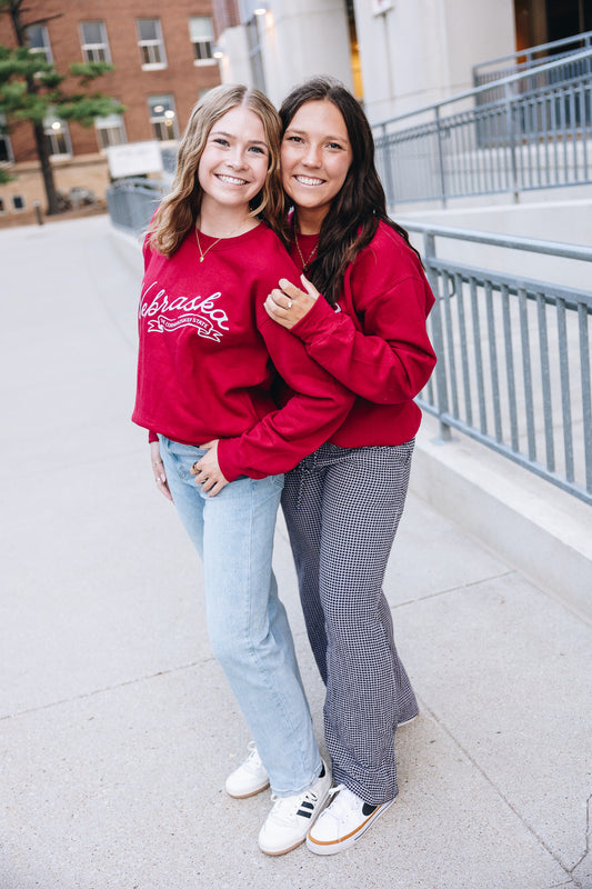 Deep red Nebraska crewneck sweatshirt with white script print, soft fabric, and relaxed fit for game day or casual wear two sizes