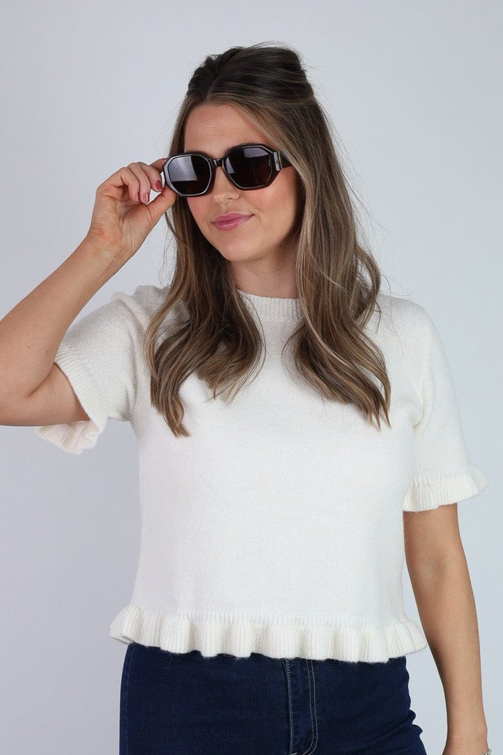 Woman wearing a white peplum top and navy pants against a plain background