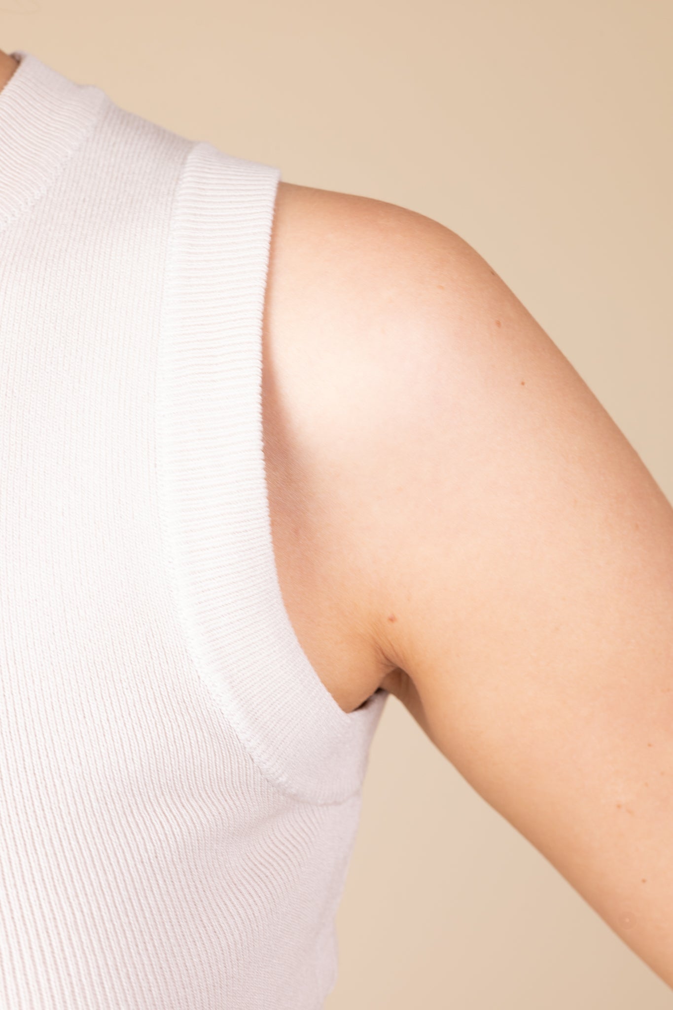 Close up detail of Cream high neck sleeveless knit top with ribbed material, offering a soft and stylish fit.