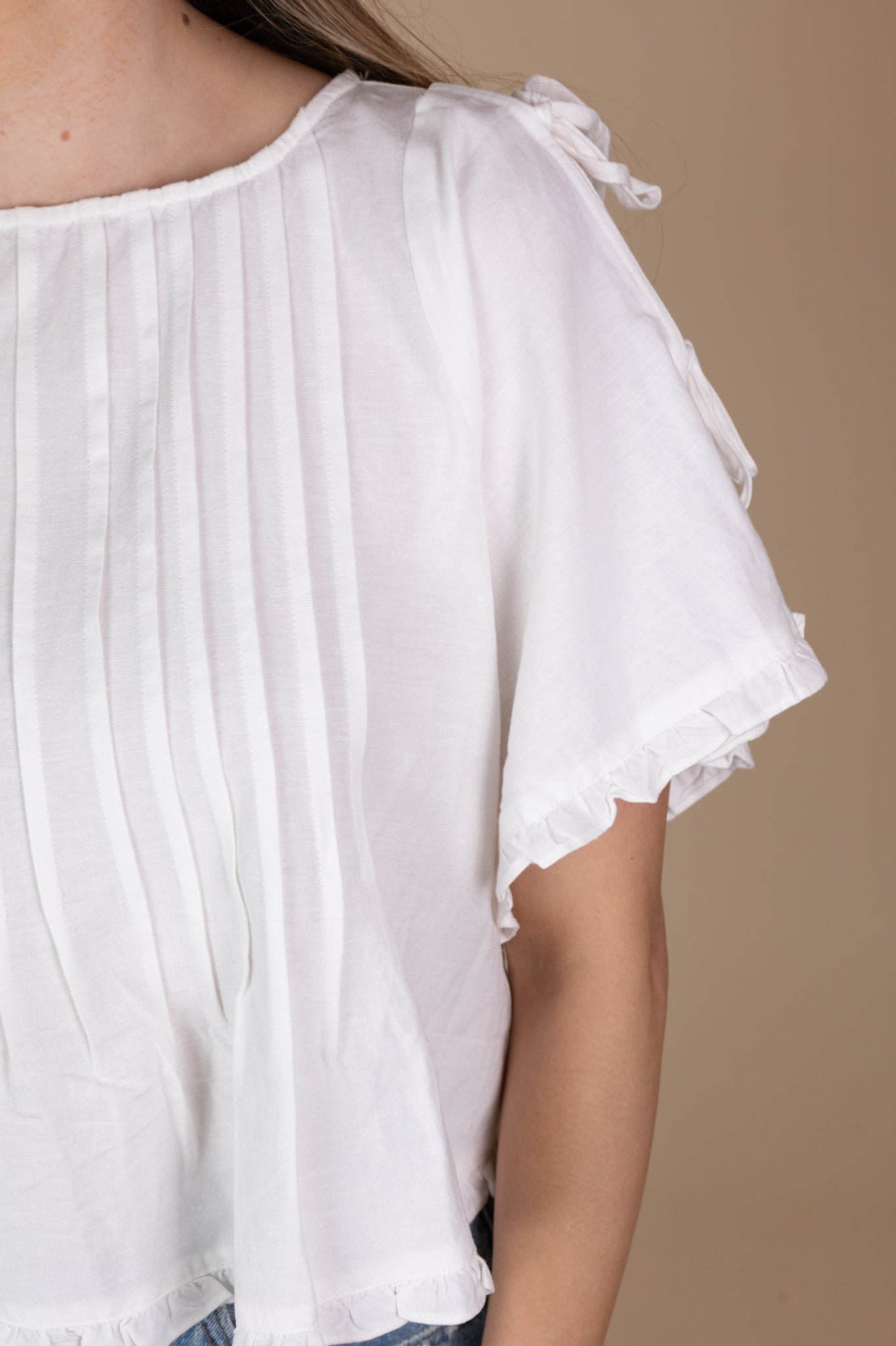 detailed view of off-white Addie Pleated Blouse with ruffle hem, tie sleeves, and pleated detailing, showcasing a loose bodice and hip-length cut.