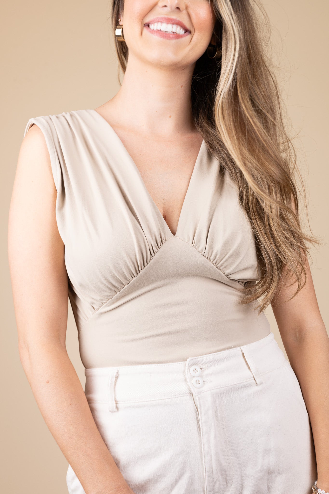 Elegant light brown Sloane plunge neck bodysuit with pleated shoulders, V neck design, and low back with tie. Ideal for special occasions and a flattering fit.