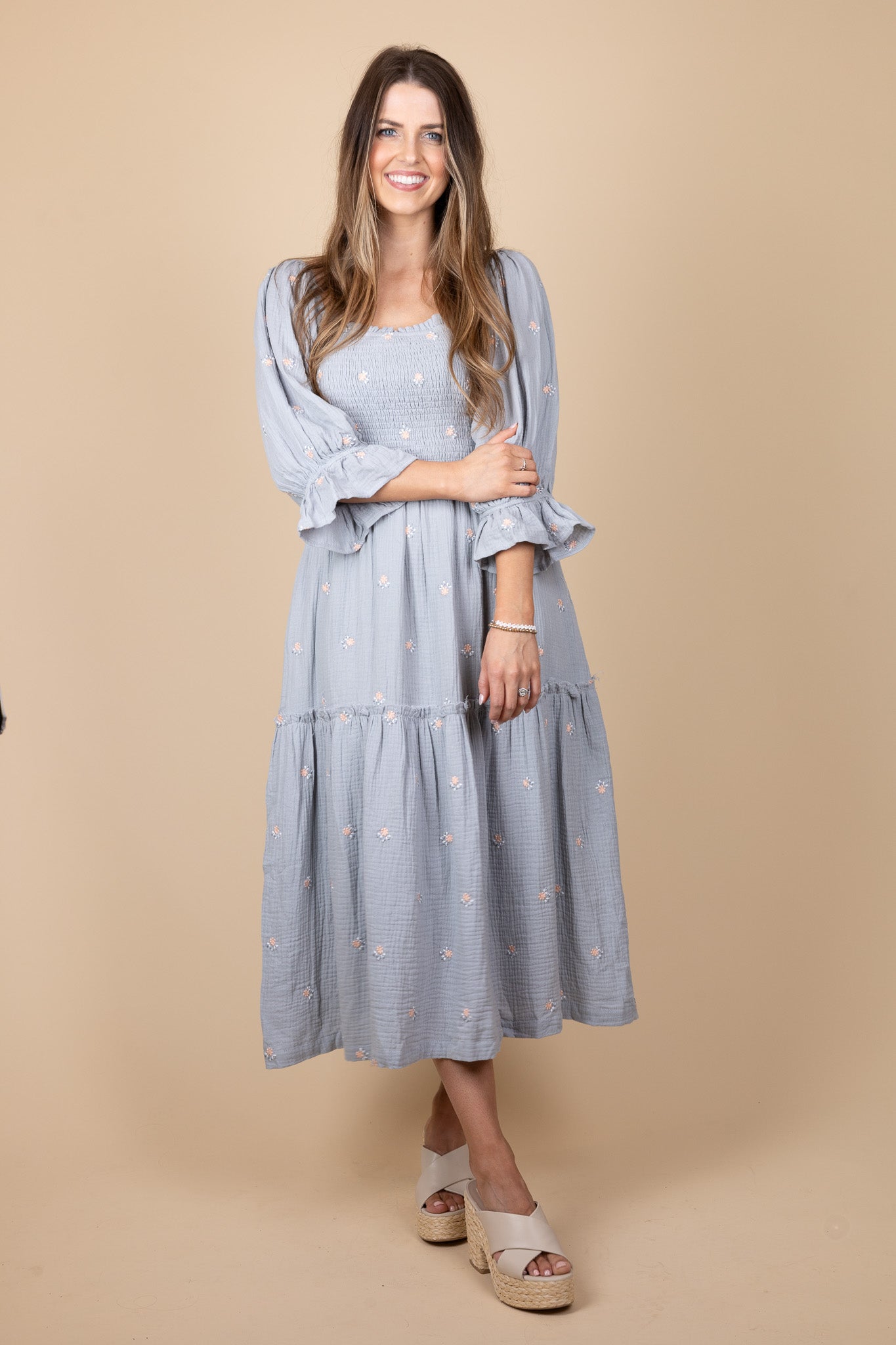 zoomed out view of Emma Floral Midi Dress with a flowy silhouette, featuring a light blue base with pink floral print, ruffle hem sleeves, and smocking through the torso. Perfect for various occasions, this midi-length dress offers a true-to-size fit.