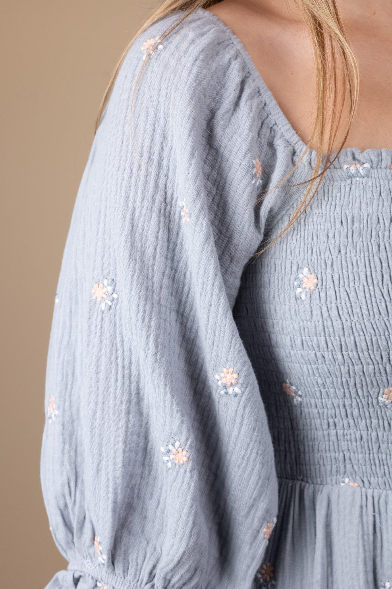 zoomed in detailed view of Emma Floral Midi Dress with a flowy silhouette, featuring a light blue base with pink floral print, ruffle hem sleeves, and smocking through the torso. Perfect for various occasions, this midi-length dress offers a true-to-size fit.