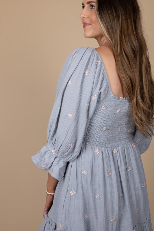 detailed view of Emma Floral Midi Dress with a flowy silhouette, featuring a light blue base with pink floral print, ruffle hem sleeves, and smocking through the torso. Perfect for various occasions, this midi-length dress offers a true-to-size fit.