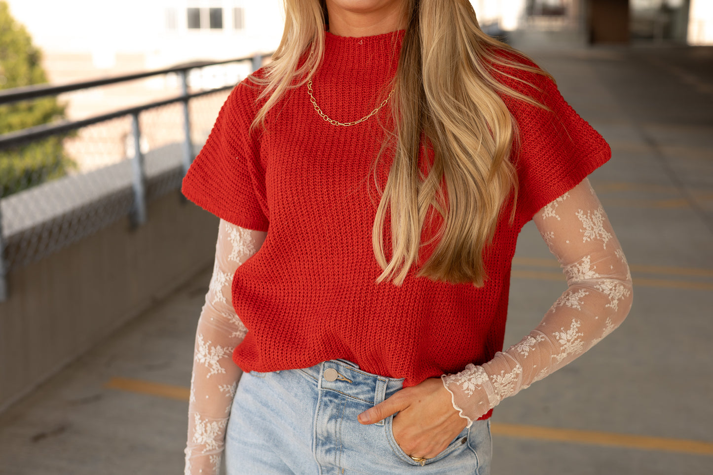 front view of red sweater vest, pocket under hair, knit material, mock neck, paired with cream lace undershirt