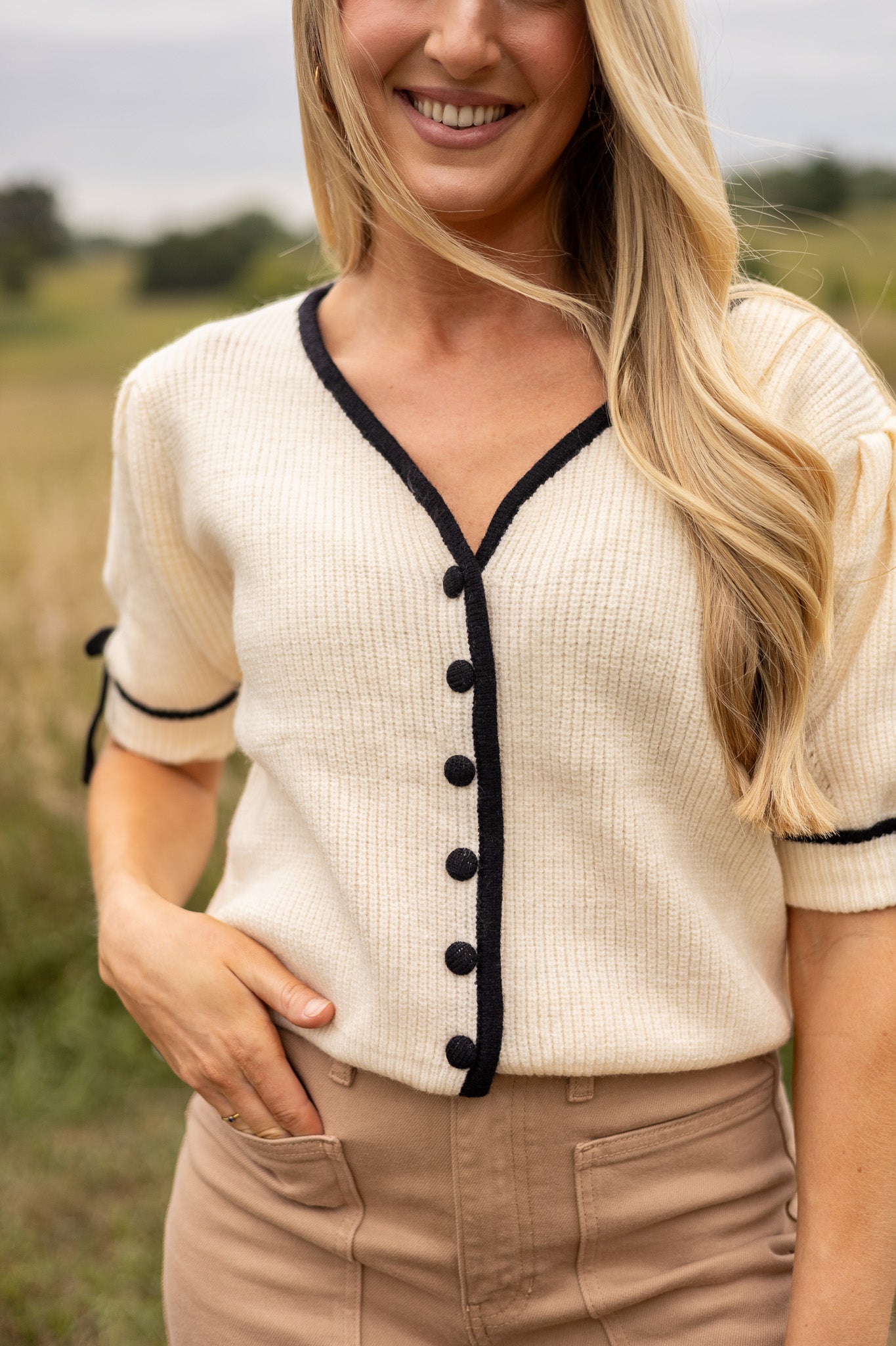 front view of cream short puff sleeve sweater with front v neck and buttons, has black trim and buttons with black tie bow on sleeves