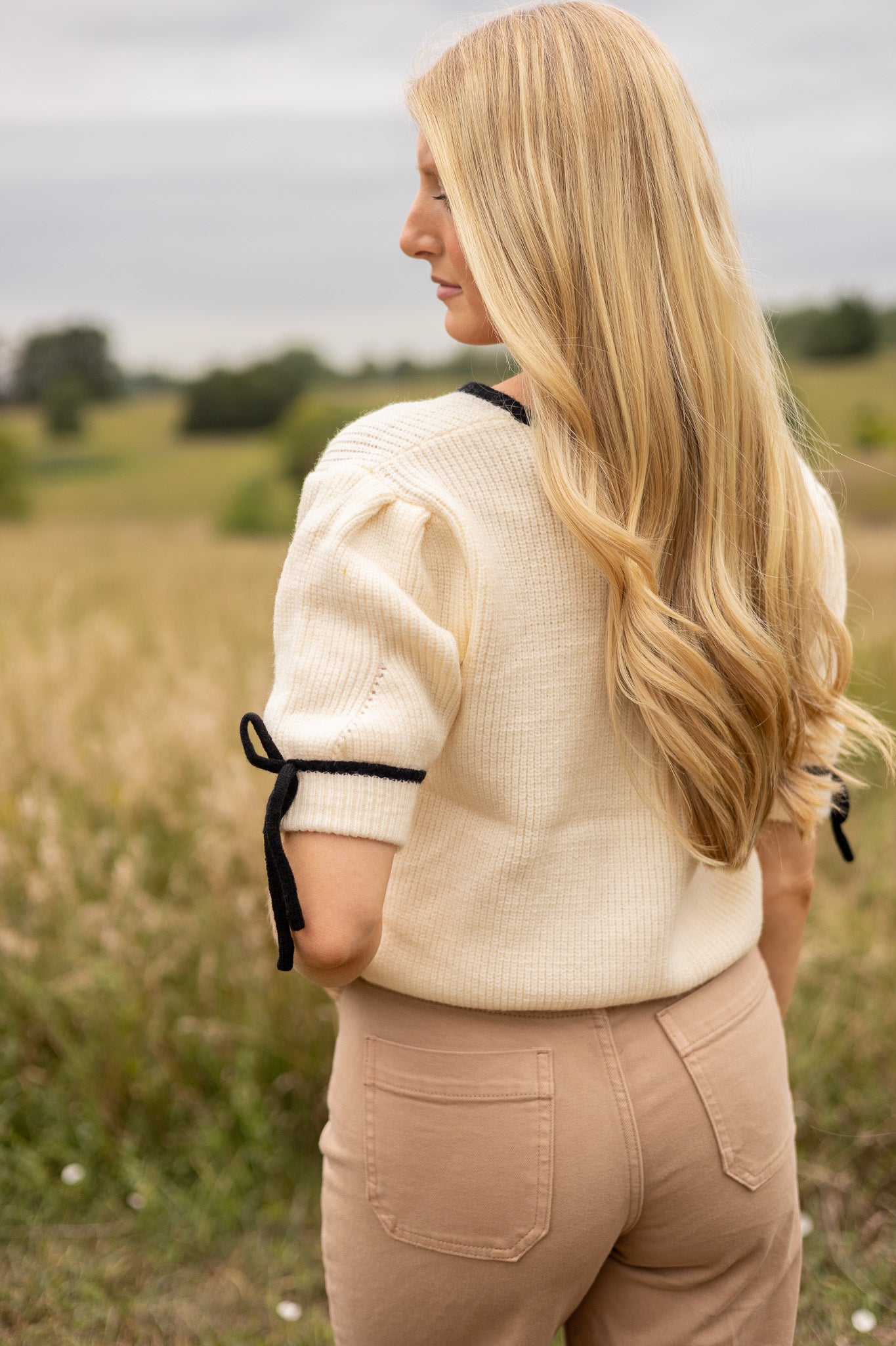 back view of cream short puff sleeve sweater has black trim with black tie bow on sleeves