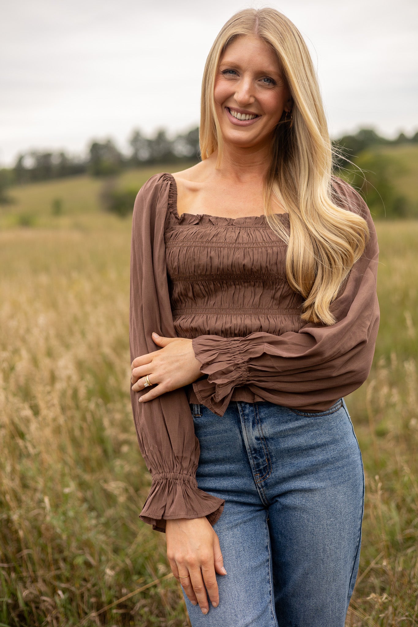 full view of brown belle sleeve top smocked bodice with ruffle trim, hip length, paired with medium wash jeans