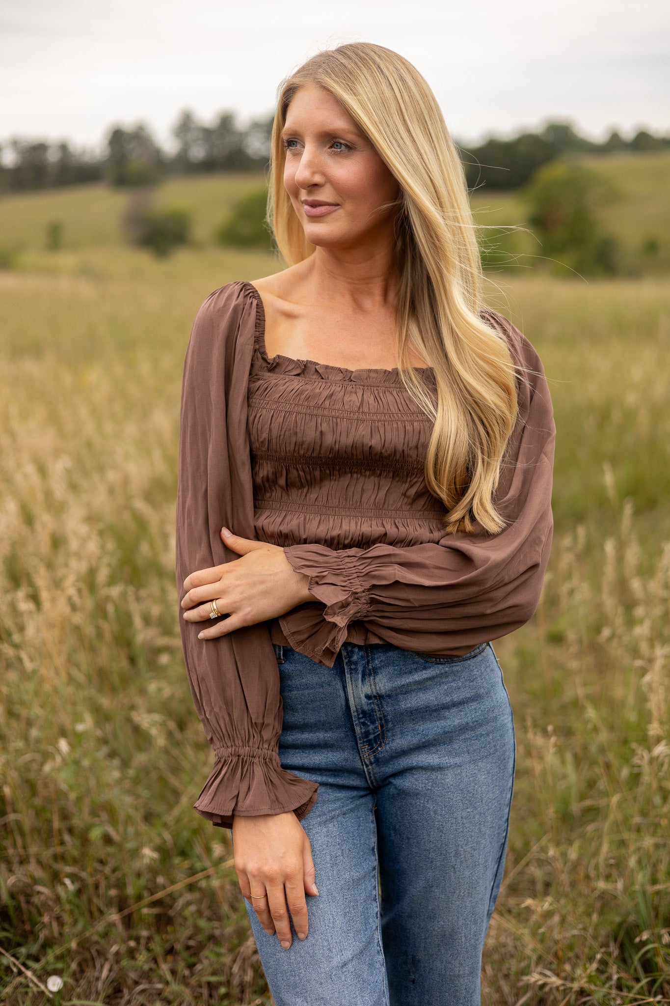 full view of brown belle sleeve top smocked bodice with ruffle trim, hip length, paired with medium wash jeans