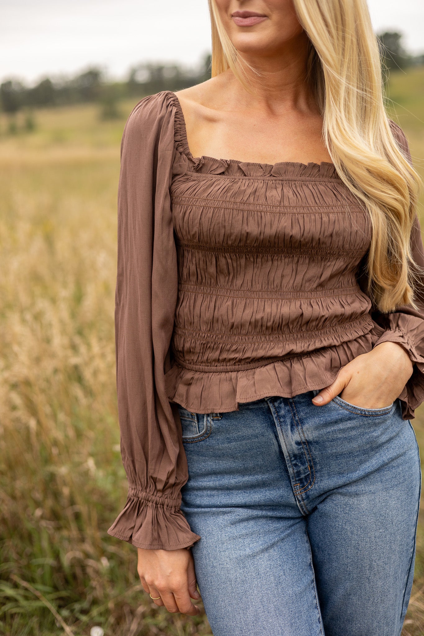 front view of brown belle sleeve top smocked bodice with ruffle trim, hip length