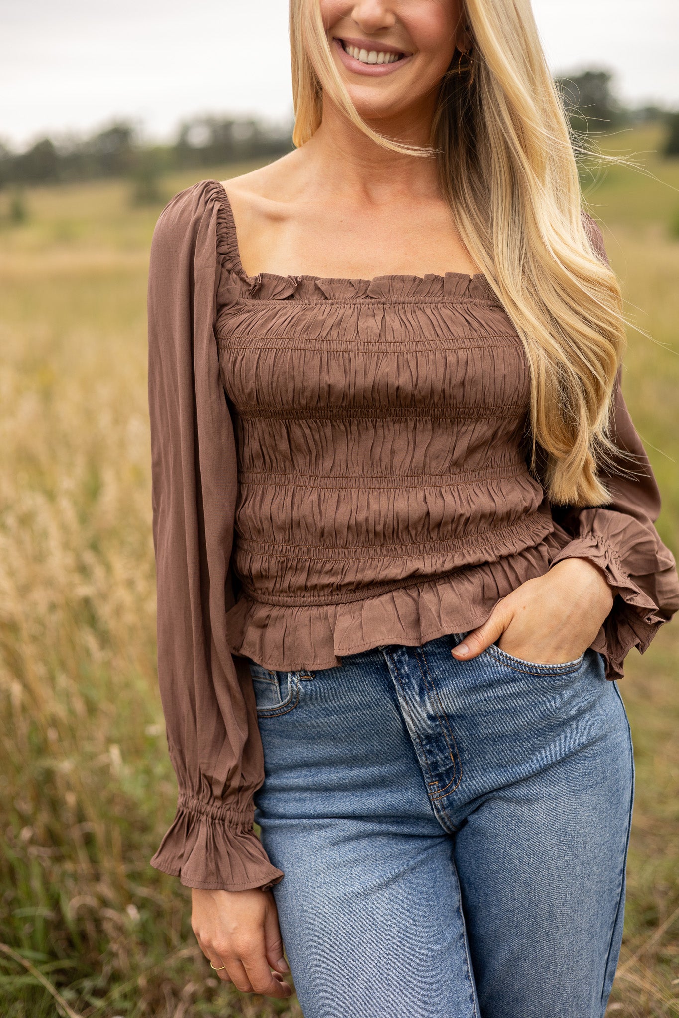 front view of brown belle sleeve top smocked bodice with ruffle trim, hip length