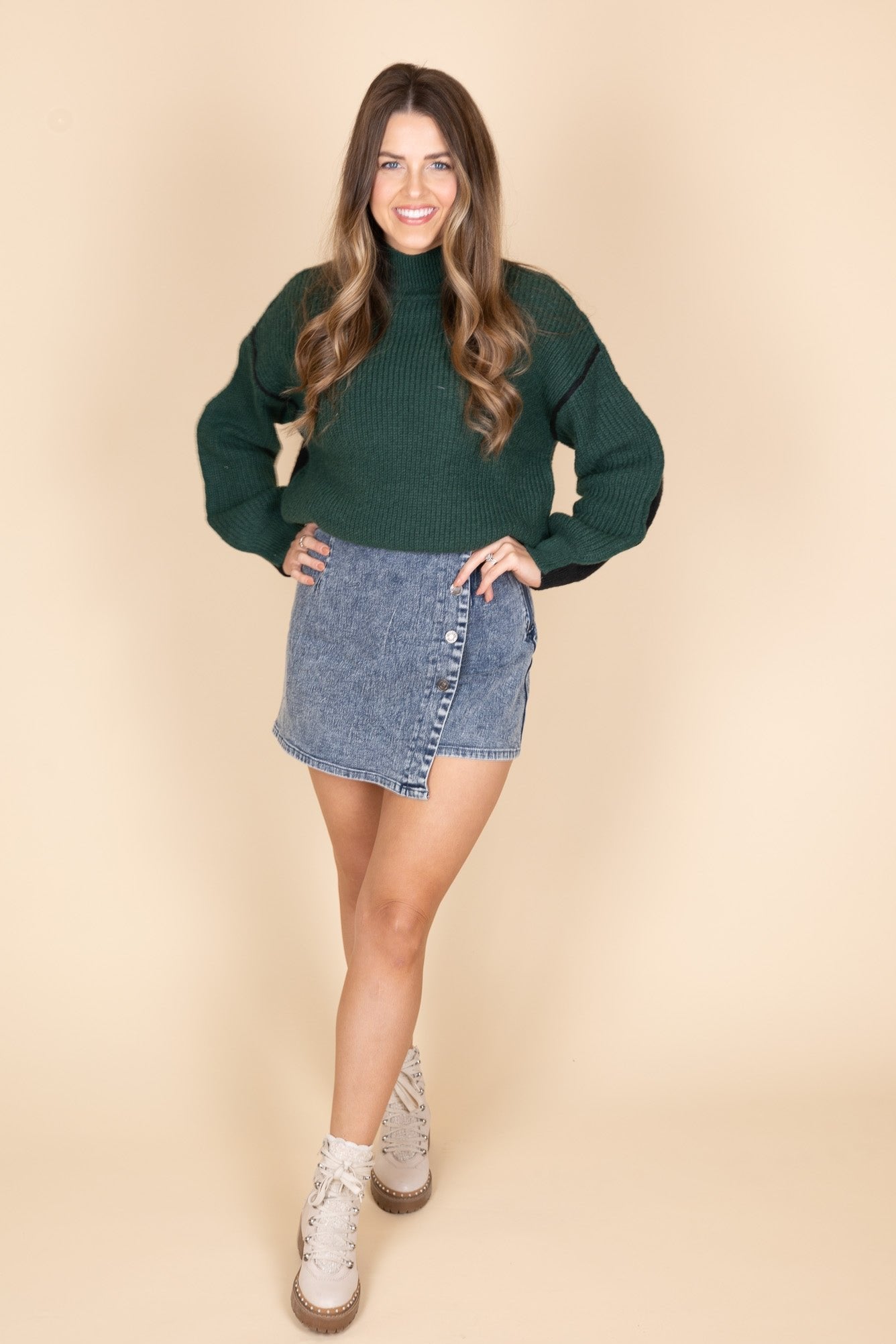 Kelly Colorblock Hunter Green and Black Sweater front view showing green in front and black in the back on the sweater. Mock neck collar design. Paired with a jean skort and cream combat boots.