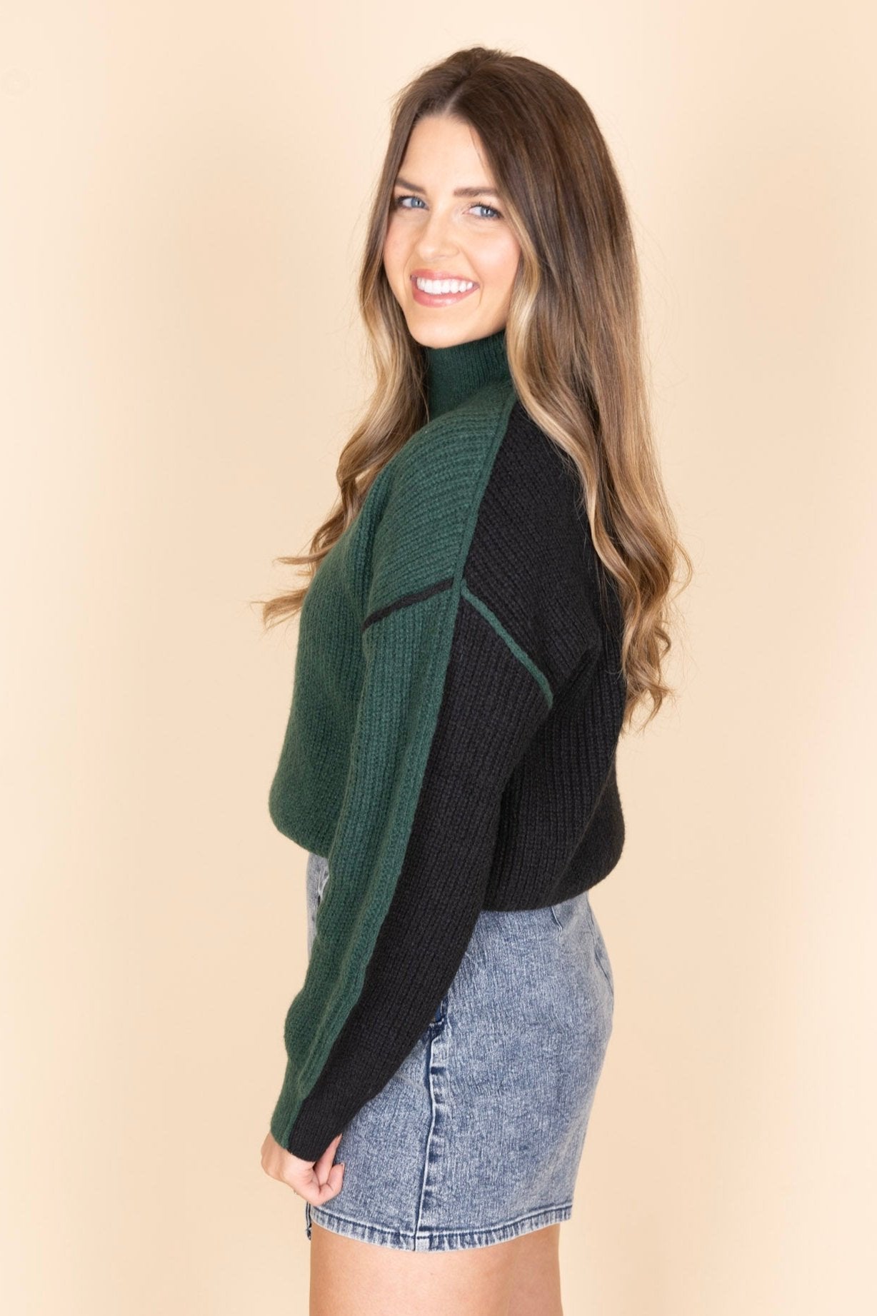 Kelly Colorblock Hunter Green and Black Sweater side view showing green in front and black in the back on the sweater. Mock neck collar design. Paired with a jean skort.