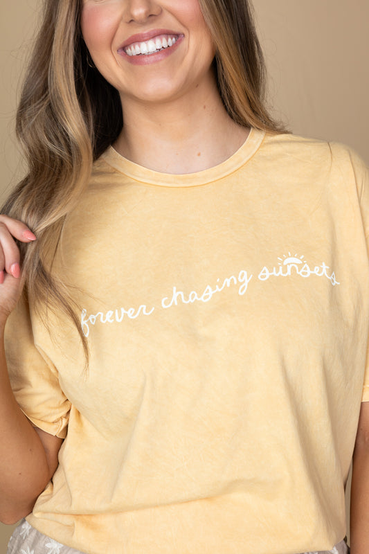 close up Chasing Sunsets Tee in golden yellow acid-washed fabric with "forever chasing sunsets" quote, soft material, full-length fit