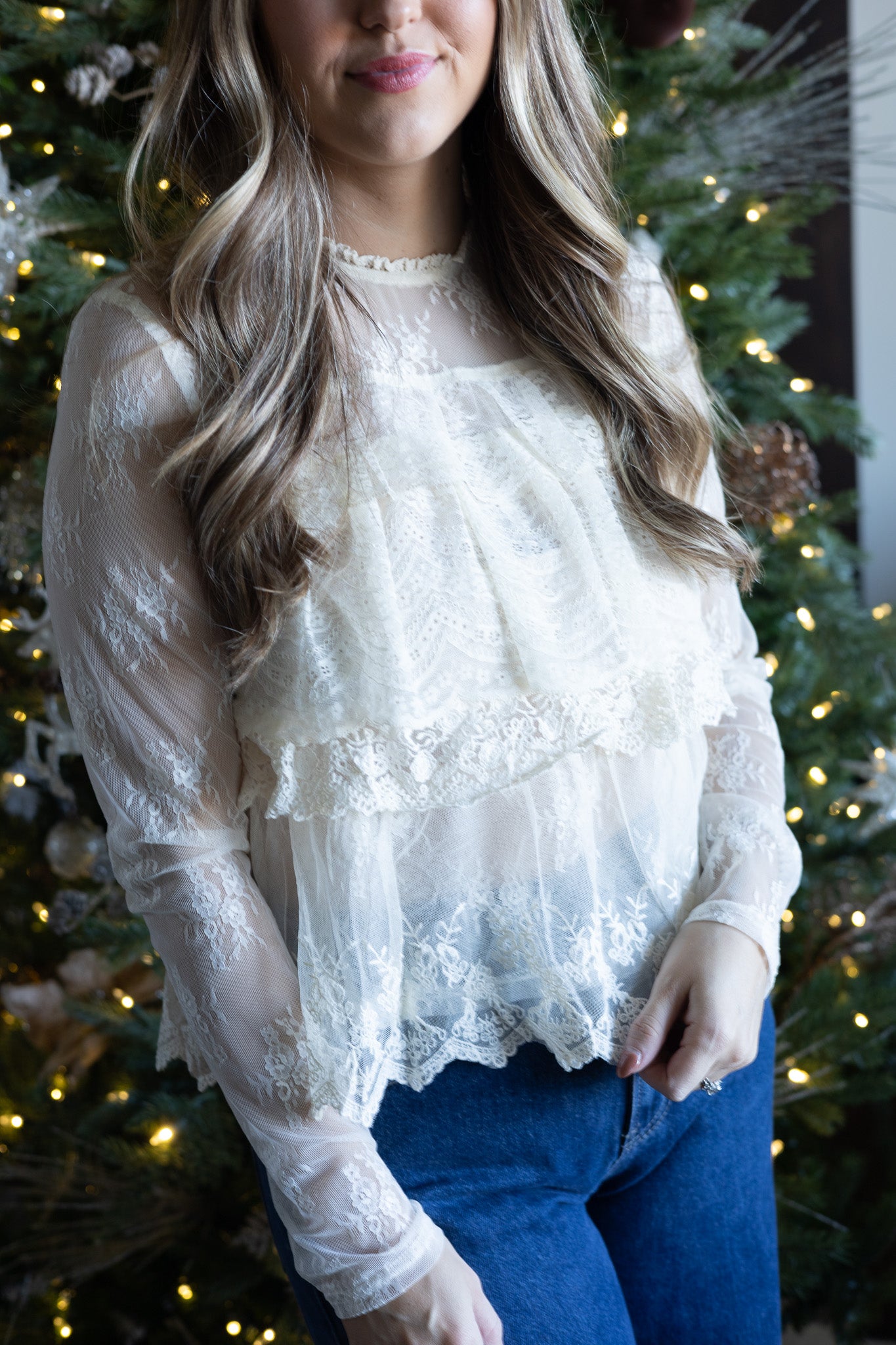 Woman wearing a white lace top with a Christmas tree in the background