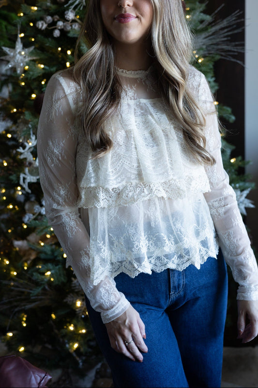 Woman wearing a lace top and blue jeans standing in front of a decorated Christmas tree.