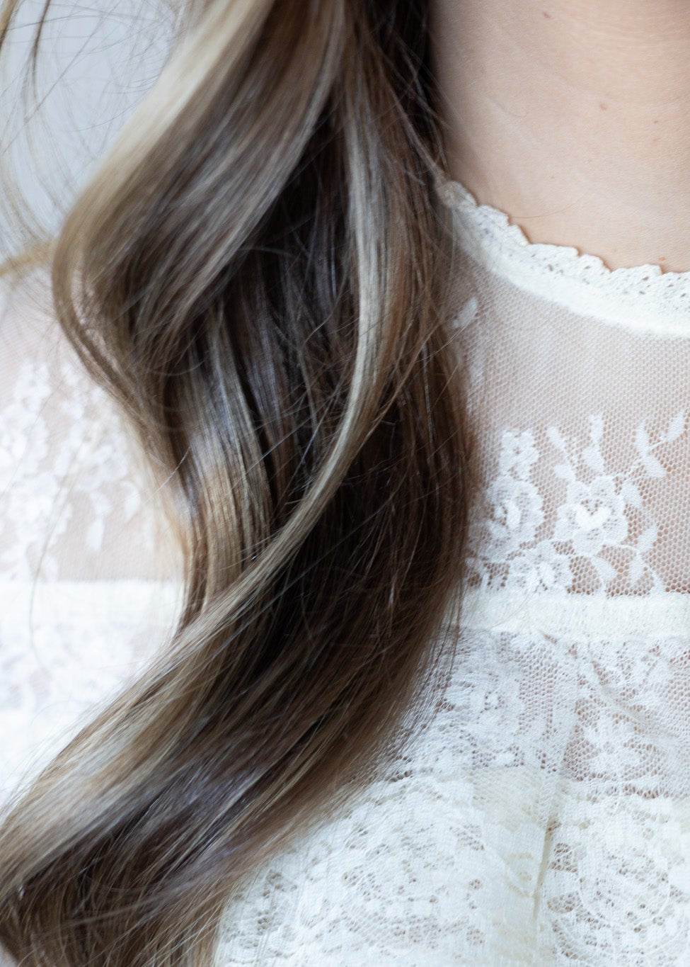 Close-up of wavy hair with a blurred white lace garment in the background