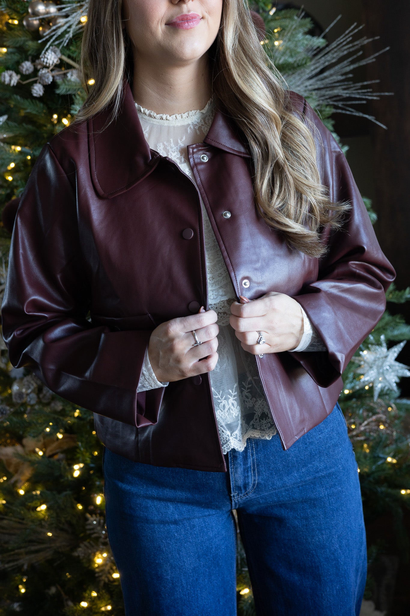 Person wearing a brown leather jacket in front of a decorated Christmas tree.