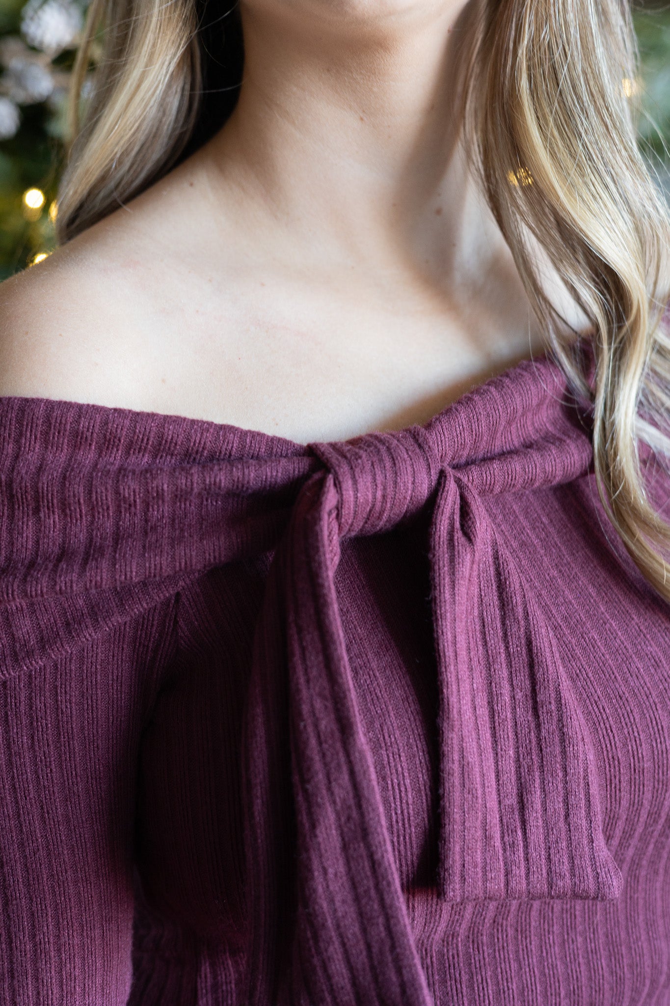 Close-up of a person wearing an off-shoulder burgandy top with a bow detail.